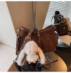 Detail of dark brown suede shoulder bag with side pockets and a plush bunny charm