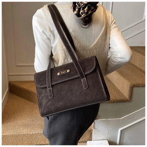 Detail of vintage brown tote bag with white contrast stitching and gold metal plaque