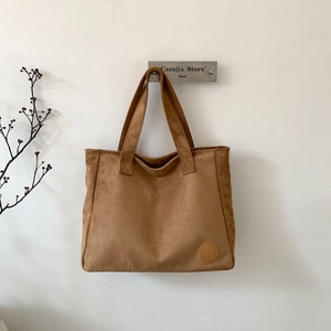 Detail view of dark brown suede tote bag with circular logo patch on white background