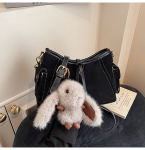 Detail of black suede shoulder bag with contrast stitching and plush rabbit charm