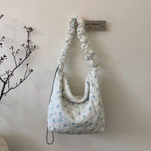 Close-up of quilted white tote bag with blue dots and elegant ruched shoulder strap detail