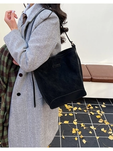 Model wearing black suede tote bag with grey herringbone coat among autumn ginkgo leaves