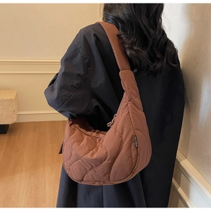 Rear view of a model wearing a brown quilted crescent bag with adjustable wide strap