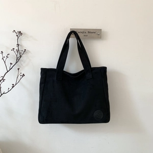 Detailed close-up of a large black matte tote bag hanging on a minimalist white wall