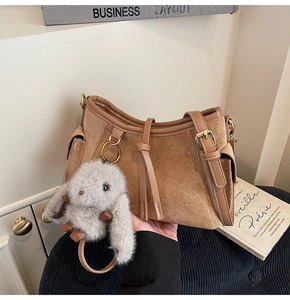 Detail of a brown suede handbag with golden hardware and plush bunny charm on books