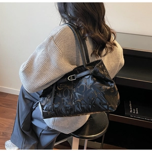 Detail of black leather tote bag featuring embossed letter patterns and metal buckles