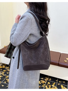 Brown suede tote bag shown on model in an autumn setting with yellow ginkgo leaves