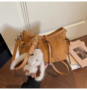 Close-up of brown suede handbag with side pocket detail and cute plush rabbit charm