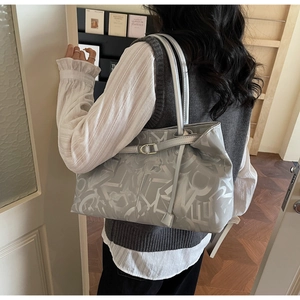 Close-up of light gray tote bag with geometric letter patterns and long shoulder straps