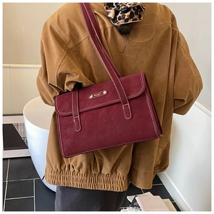 Detail of burgundy leather shoulder bag with white contrast stitching and gold metal logo