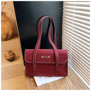 Close-up of burgundy suede shoulder bag with gold metal plate on a wooden desk