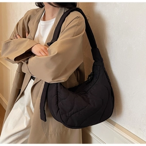 Detailed view of black quilted half-moon shoulder bag worn by model in trench coat