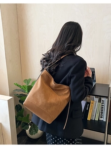 Close-up of brown suede shoulder bag worn by model in a minimalist library setting
