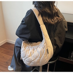 Detail of quilted beige puffer shoulder bag with wide strap on model