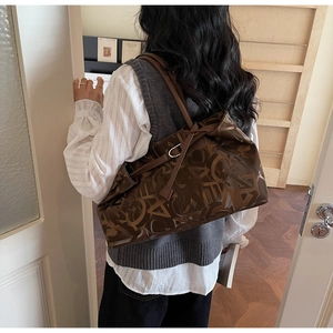 Detailed view of brown leather tote bag with vintage letter print worn by a model