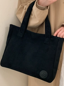 Large black minimalist tote bag with circular logo badge worn with khaki trench coat