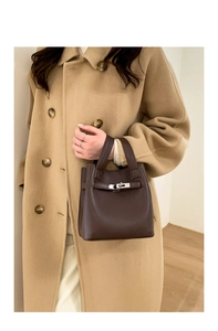 Detail view of dark brown pebbled leather handbag held by model in khaki coat