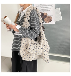 Detail of plush cream shoulder bag featuring blue floral patterns and a large decorative bow