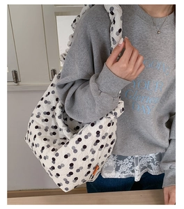 Detail shot of the textured polka dot fabric and orange logo tag on a white shoulder bag