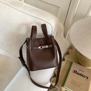 Detail of dark brown lychee grain leather bucket bag with silver lock on white sofa