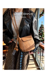 Detail of a brown leather bucket bag featuring drawstring closure and spherical tassel charm