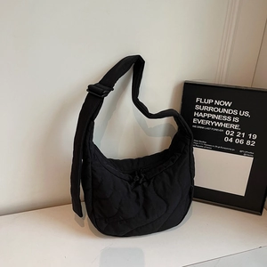 Detail of black quilted crescent shoulder bag featuring adjustable strap and wavy pattern