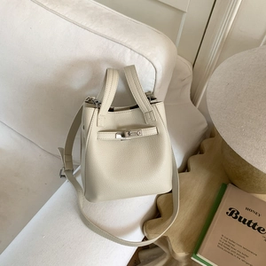 Close-up of beige lychee grain leather bucket bag with silver twist lock and strap