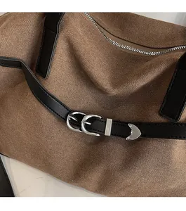 Detail of tan canvas tote bag with black leather trim and silver metal hardware buckles
