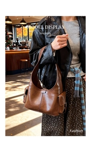 Brown leather underarm hobo bag shown on model in a warm cafe lifestyle setting