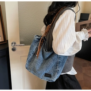 Detail of blue denim tote bag with thick brown rope strap and branded leather label