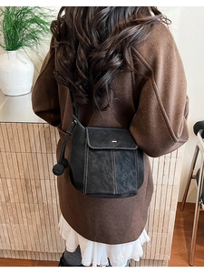 Close-up of black bucket bag featuring contrast white stitching and round charm detail