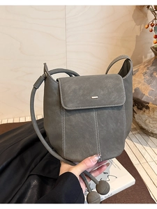Detailed view of grey bucket bag showing contrast white stitching and gold metal plate