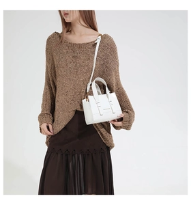 Close-up of white leather square bag worn cross-body over a brown knit sweater