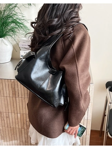 Detail view of the sleek black glossy PU leather shoulder bag on a model in wool coat