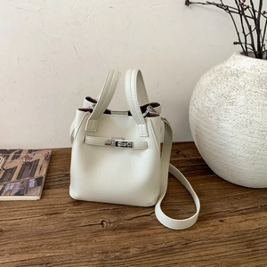 Close-up of cream lychee grain leather bucket bag with silver metal lock on wood table