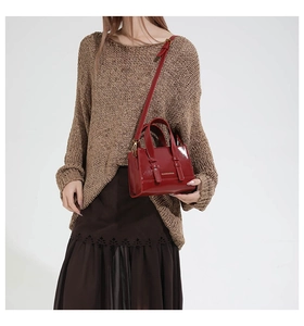 Close-up of a red patent leather crossbody bag styled with a brown knit sweater