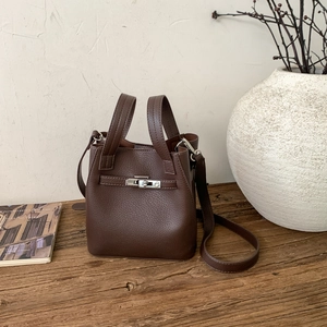 Detailed view of dark brown pebbled leather bucket bag with metallic twist-lock on wood table