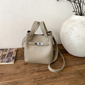 Detail of minimalist beige bucket bag with silver turn-lock clasp on a vintage desk
