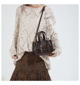 Detail of dark brown leather crossbody bag with gold logo on beige knit sweater outfit