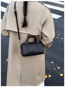 Street style shot of a woman with black pebble leather Boston bag and beige trench coat
