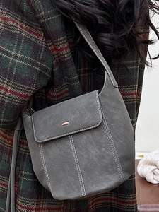 Retro grey matte bucket bag with white stitching and metal detail on plaid coat