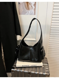 Detail view of black leather shoulder bag with side flap pockets on a grey suitcase