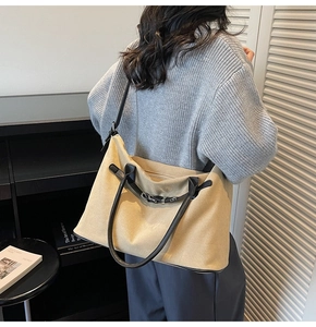Detail of a large beige suede tote bag with black leather straps on a modern background