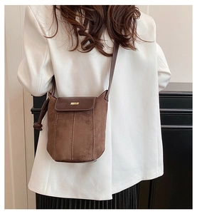 Brown suede crossbody bucket bag with white stitching and gold buckle worn with white suit