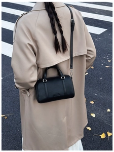 Detailed view of black litchi pattern Boston bag worn with a khaki trench coat