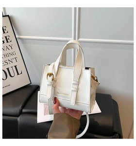 Detail of white patent leather shoulder bag featuring gold hardware and fashion lettering