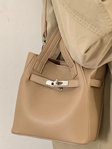 Elegant camel leather bucket bag with top handle and silver buckle on wool coat background