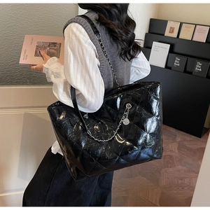 Detail of a large black quilted tote bag with silver chain strap and shiny wax leather texture