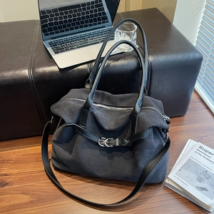 Detail of grey canvas tote bag with black leather straps and buckle on wooden floor