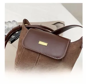 Detail view of brown suede bucket bag with contrast stitching and gold metal fastener